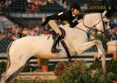 a woman riding on the back of a white horse in front of an arena full of people