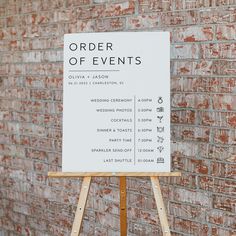 a white sign sitting on top of a wooden easel in front of a brick wall