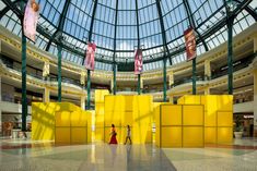 two people are walking in the middle of a large building with yellow walls and glass ceiling