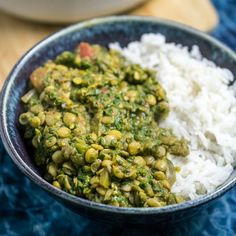 a bowl filled with white rice and green vegetables next to a spoon on a blue table cloth