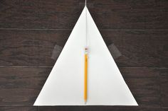 an origami paper airplane with a pencil sticking out of the side on a wooden floor