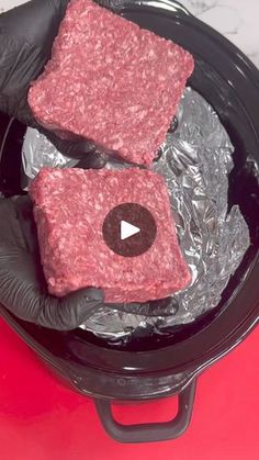 two raw hamburger patties in a slow cooker with black gloved hands on top