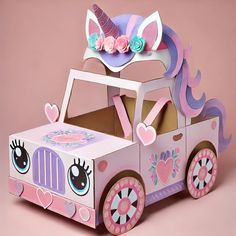 a paper car with a unicorn hat on top and flowers in the back, is made out of cardboard