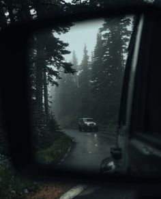 a car is seen in the rear view mirror as it drives down a road through some trees