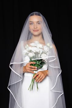 a woman in a white wedding dress holding a bouquet of flowers and wearing a veil