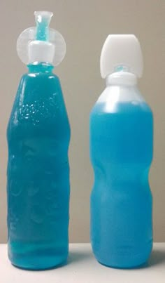 two blue water bottles sitting next to each other on a white counter top, one is empty and the other has a straw in it's cap