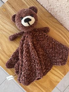 a crocheted brown teddy bear laying on top of a wooden table next to a wall