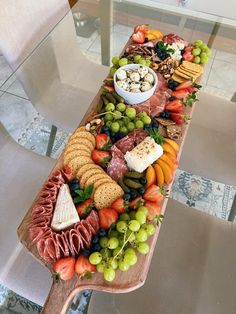 a wooden table topped with lots of different types of cheese and crackers next to a bowl of fruit