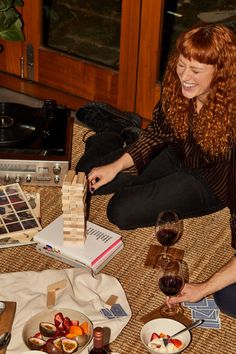 a woman sitting on the floor with some food and wine