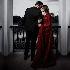 a man and woman dressed in red are standing on a balcony looking at each other