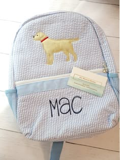 a blue and white backpack with a yellow dog on it's front pocket, along with a name tag that says mac