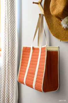 an orange and white bag hanging on the wall next to a hat rack with a straw hat