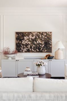 a living room with white furniture and a painting on the wall above it's coffee table