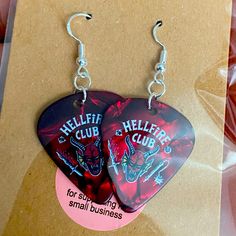 two guitar picks with the words hellfire club on them are hanging from earrings hooks