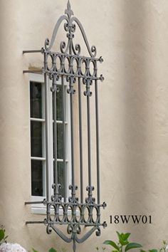 a wrought iron window on the side of a building with flowers in front of it