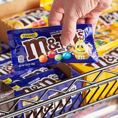 a person holding a bar of m & m's candy in front of a shelf