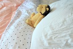 a teddy bear is laying in bed with its head on the pillow