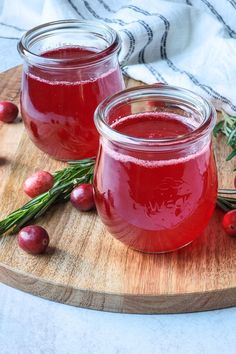 two jars filled with cranberry juice sitting on top of a wooden cutting board