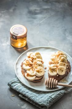 a plate topped with two sandwiches covered in banana slices and peanut butter next to a jar of honey