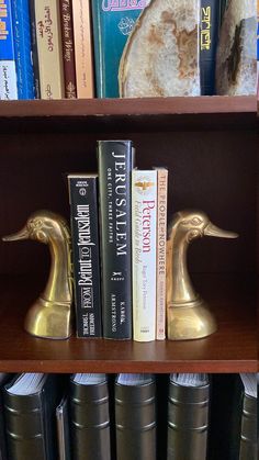 some books are sitting on a shelf in front of the bookshelf with two golden ducks