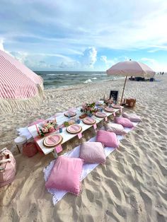 a table set up on the beach with pink and white pillows