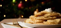 a white plate topped with dumplings next to a fork and christmas tree in the background