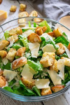 a salad in a glass bowl with cheese and dressing on the side next to bread