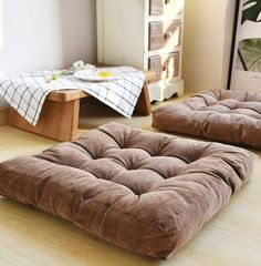 two brown futons sitting on top of a hard wood floor next to a table