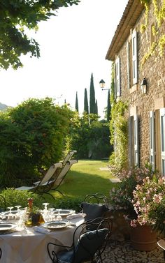 an outdoor dining area in front of a stone building with potted plants on the patio