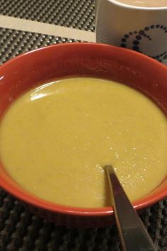 a red bowl filled with soup next to a white cup on top of a table