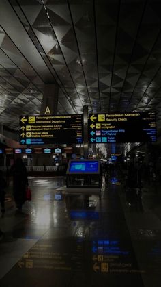 an airport terminal with many signs and people walking through the walkways at night time