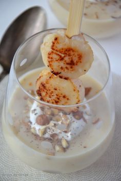 two desserts with bananas and nuts in a glass on a white tablecloth next to a spoon