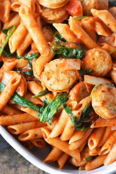 a white bowl filled with pasta and meat covered in tomato sauce, spinach and cheese