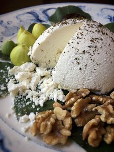 an assortment of cheeses and nuts on a blue and white plate with green leaves