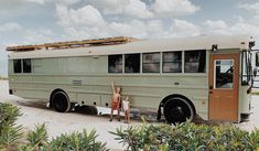 two people standing in front of an old bus on the beach with their arms up