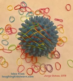 a bunch of colored paper clips sitting on top of a white table next to a ball of yarn