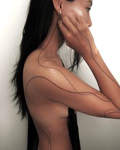 a woman with lines painted on her back and shoulder, holding her hand to her face