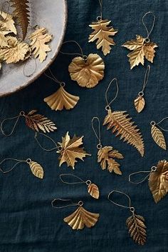 gold leaf ornaments on a blue table cloth next to a white bowl and silver plate