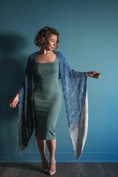 a woman in a green dress and blue shawl is standing on a wooden floor