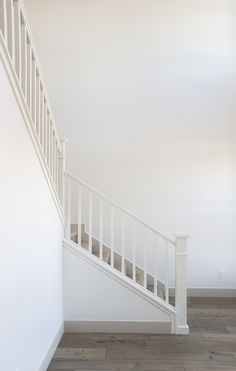 an empty room with white walls and wooden flooring is pictured in this image, there are stairs leading up to the second floor