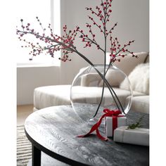 a glass vase filled with red berries on top of a table next to a white couch