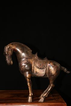 a bronze statue of a horse standing on top of a wooden table next to a black wall