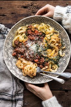 a bowl filled with pasta and meat sauce on top of a wooden table next to a fork