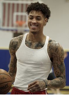 a man with tattoos holding a basketball in his hand and smiling at the camera while wearing red shorts