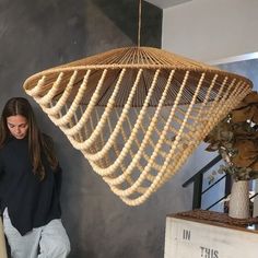 a woman standing in front of a wooden light fixture with rope hanging from the ceiling