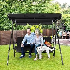 a man and woman sitting on a swing with a dog in the grass next to them