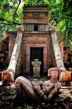 a statue sitting in front of a building surrounded by trees and bushes with an open doorway