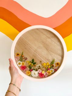 a person holding up a bowl with flowers in the center and a rainbow painted wall behind it