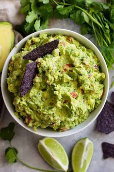 a bowl filled with guacamole surrounded by tortilla chips and limes