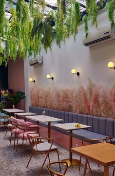 an empty restaurant with pink chairs and plants hanging from the ceiling, along with long tables